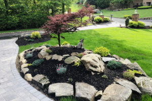 A photo of a landscaped property including grass, rocks, mulch, and trees.