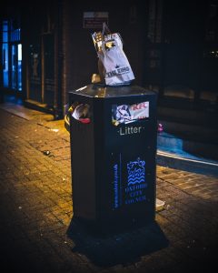 A photo of a property with an overflowing trash can with a bag placed on the lid.