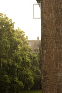 A photo of a bright but raining sky with a building and a tree. It looks like a summer rain!